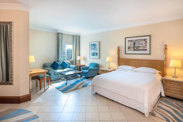 Hotelzimmer im Sheraton Jumeirah Beach Resort mit Doppelbett, Sofa, Tisch und Dekor.