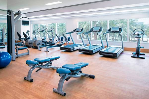 Fitness-Center im Sheraton Jumeirah Beach Resort mit vielen Geräten und großen Fenstern.
