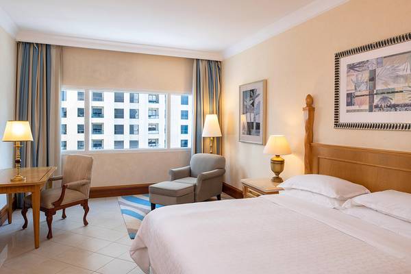 Schlafzimmer im Sheraton Jumeirah Beach Resort mit Bett, Lampen und Fenstern.