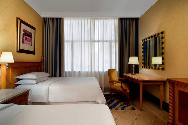 Zwei Betten in einem Hotelzimmer des Sheraton Jumeirah Beach Resort mit Schreibtisch und Lampe.