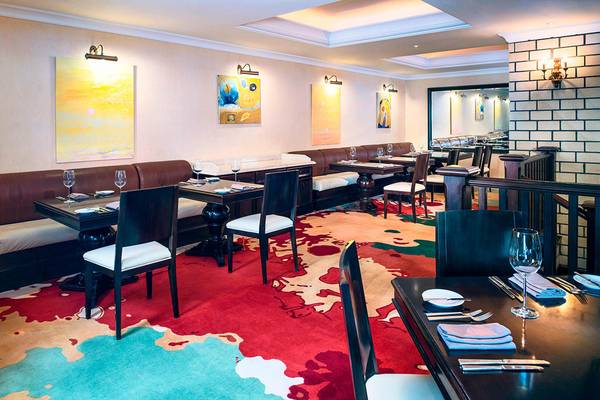 Restaurant im Sheraton Jumeirah Beach Resort mit gemustertem Teppich, dunklen Tischen und Stühlen.