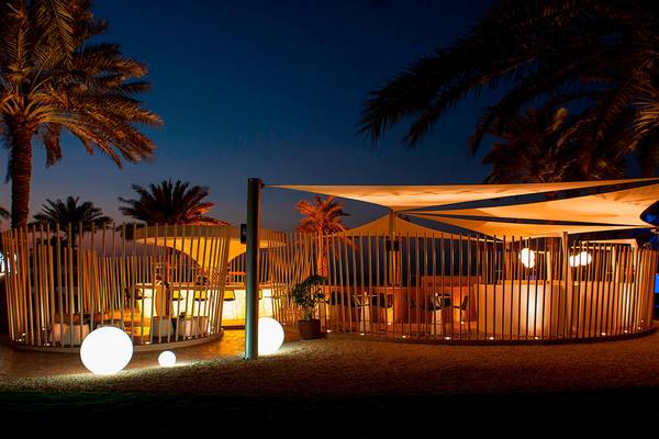 Nachtansicht der Strandbar des Sheraton Jumeirah Beach Resorts mit beleuchteten Lampen und Schatten unter Palmen.
