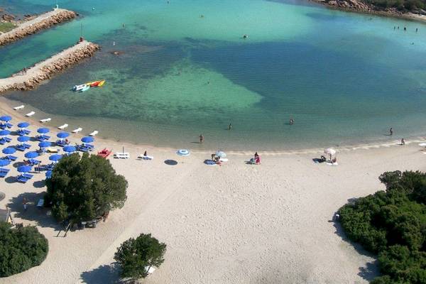 Luftaufnahme des Hotel Ollastu Resorts mit weißer Strand, blauen Sonnenschirmen und Menschen im Wasser.