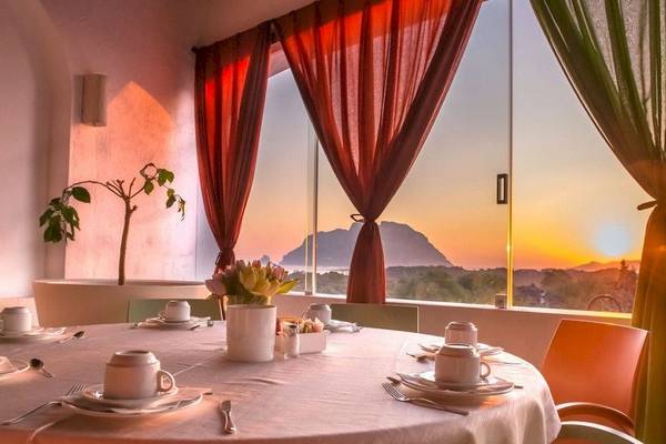 Speisezimmer im Hotel Ollastu Resort mit Tisch, Blick auf einen Berg und den Sonnenuntergang.