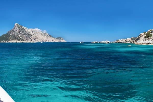 Aussicht auf das Meer vom Hotel Ollastu Resort mit kristallklarem Wasser und Bergen im Hintergrund.