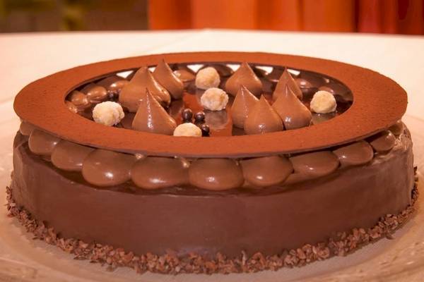 Ein Schokoladenkuchen mit Schokoladenherzen und Makronen obenauf, auf einem Glasteller serviert.