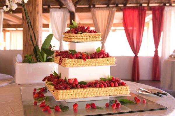 Eine dreistöckige Hochzeitstorte im Hotel Ollastu Resort mit Früchten und Blättern verziert.