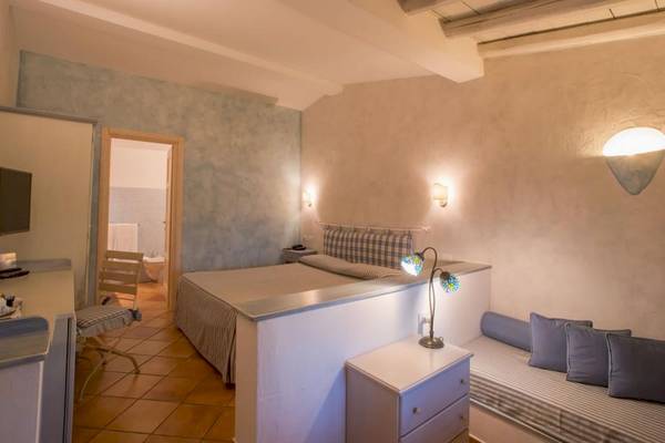 Innenansicht eines Hotelzimmers im Ollastu Resort mit Bett, Sofa, Nachttisch und Badezimmertür