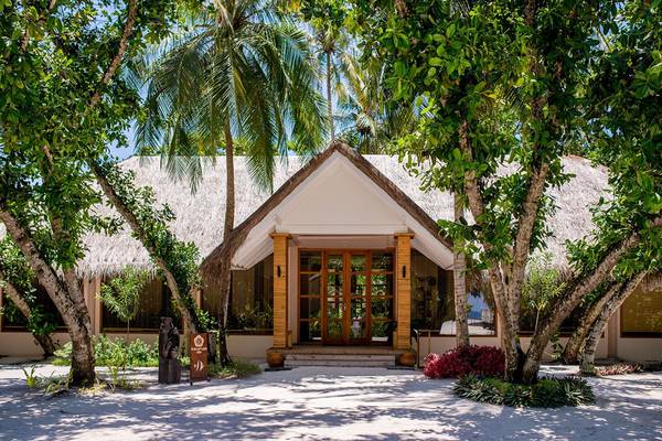 Außenansicht des Kudafushi Resort & Spa mit einem strohgedeckten Dach und Glastüren.