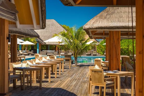 Außenbereich des Kudafushi Resort & Spa Restaurants mit Holztischen und Stühlen.