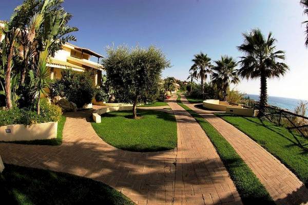 Außenbereich des Cala di Volpe Hotels mit gepflasterten Wegen und grünen Rasenflächen.