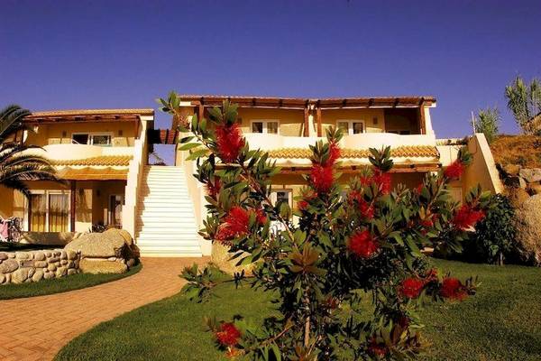 Außenansicht des Cala di Volpe Hotels mit roten Blumen im Vordergrund.