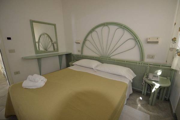 Ein Schlafzimmer im Hotel Cala di Volpe mit grünem Kopfteil, Bettwäsche und Spiegel