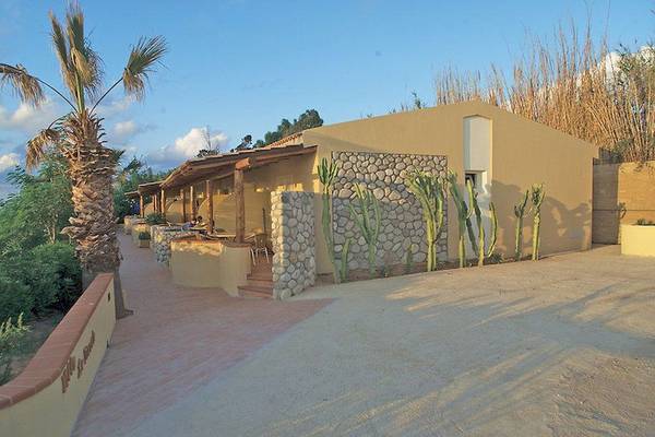 Außenansicht des Cala di Volpe Hotels mit Steinmauer und Kakteen.