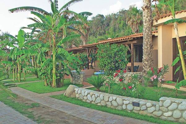 Außenbereich des Cala di Volpe Hotels mit Blumen, Palmen und Steinmauer.