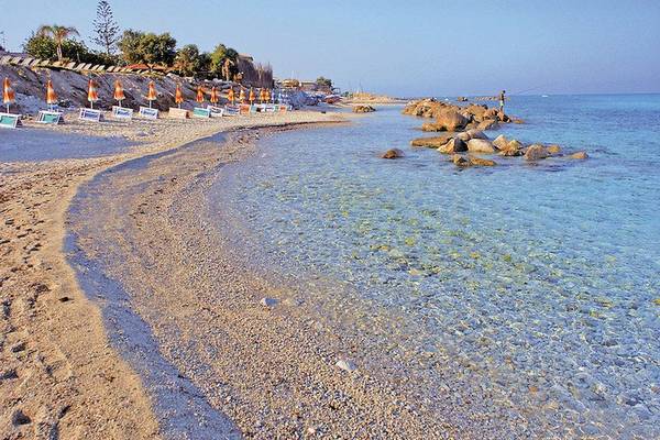 Strand von Cala di Volpe mit Fischer im Wasser, umgeben von Felsen und Sonnenschirmen.