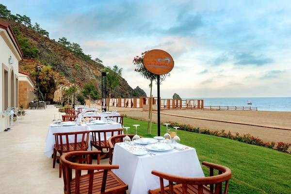 Terrasse des Rixos Premium Tekirova Hotels mit Blick auf das Meer und gedeckten Tischen.