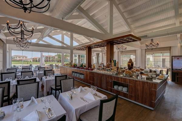 Innenansicht des Restaurants im Rixos Premium Tekirova Hotel mit Tischplatten, Stühlen und einem großen Buffet.