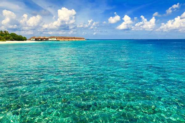 Außenansicht des Kudafushi Resort & Spa mit Blick auf das kristallklare Meer.