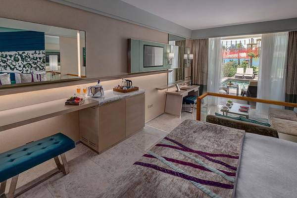 Innenansicht eines Hotelzimmers im Rixos Premium Tekirova mit Bett, Schreibtisch und Aussicht auf den Pool.