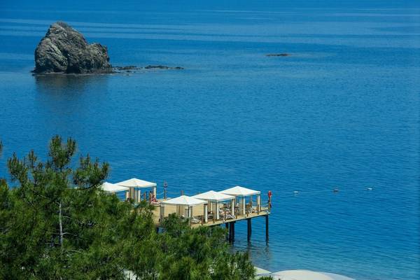 Luftaufnahme des Rixos Premium Tekirova Strandes mit Wasser, Felsen und Sonnenschirmen