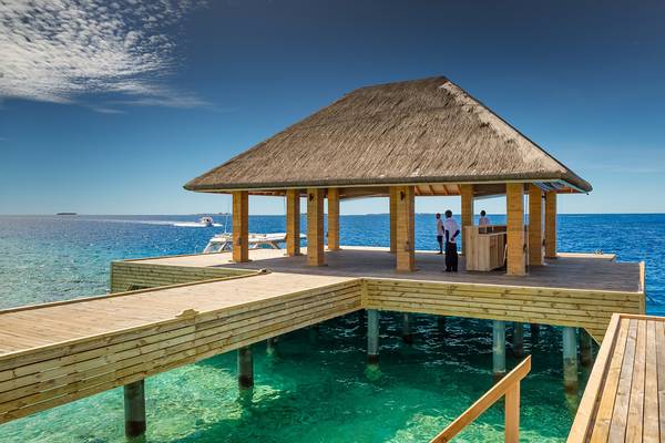 Pavillon am Strand des Kudafushi Resorts & Spa mit drei Personen, die auf einer Plattform stehen.