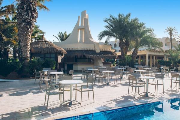 Pool-Loungebereich des Iberostar Mehari Djerba Hotels mit Tischen, Stühlen und Sonnenschirmen.