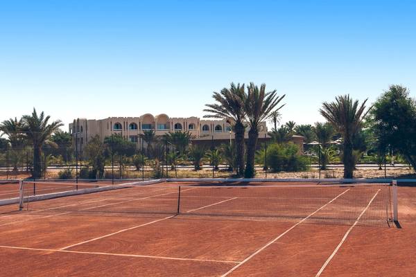 Tennisplatz im Iberostar Mehari Djerba Hotel mit Palmen und Gebäude im Hintergrund.