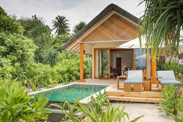 Außenbereich des Kudafushi Resort & Spa mit einer kleinen Hütte, Swimmingpool, Sonnenliegen und einem Schirm.
