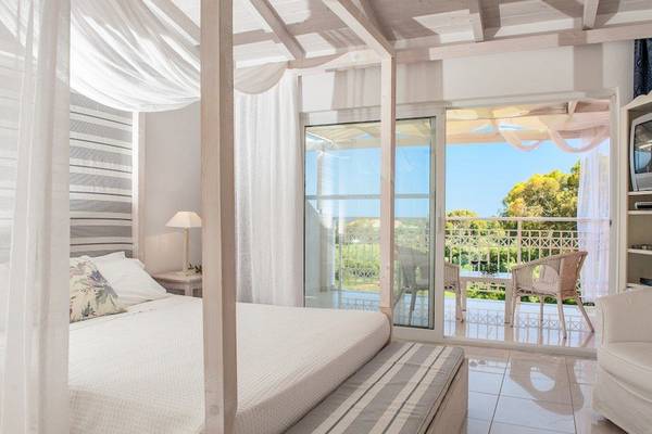 Schlafzimmer mit Balkon im Belvedere Luxury Suites, zeigt ein Himmelbett mit Baldachin, Blick auf eine Terrasse mit Möbeln.