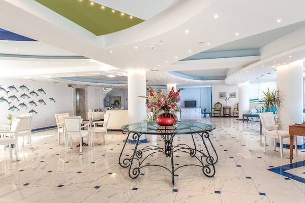 Foyer des Belvedere Luxury Suites Hotels mit einem Tisch, Blumen und weißen Stühlen.