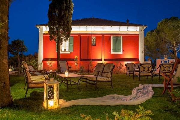 Ein rotes Gebäude namens Belvedere Luxury Suites beleuchtet am Abend mit einem ruhigen Garten davor.