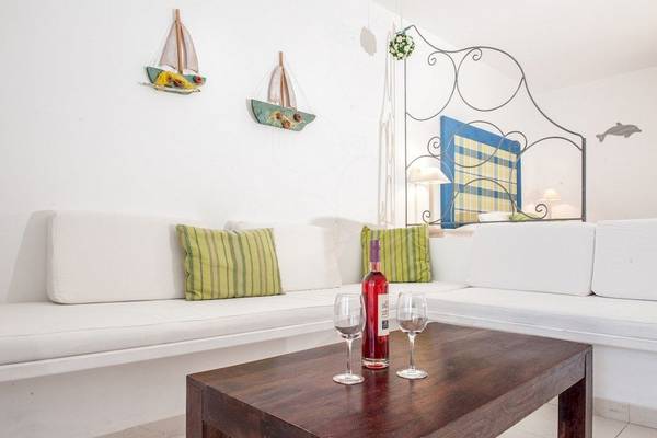 Wohnzimmer mit weißem Sofa, grünen Kissen und Weinflasche auf Holztisch.