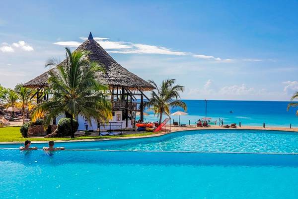 Zwei Personen schwimmen im Pool des Royal Zanzibar Beach Resorts, das von Palmen umgeben ist.