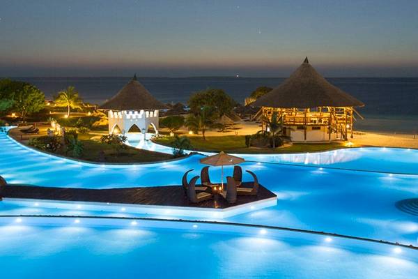 Ein Swimmingpool im Royal Zanzibar Beach Resort bei Nacht, mit illuminierten Gebäuden und einem Strand im Hintergrund.