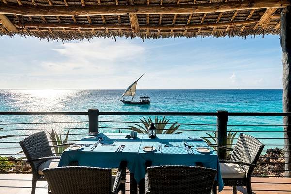 Tisch auf der Terrasse im Royal Zanzibar Beach Resort mit Blick auf das Meer und eine Dhow.