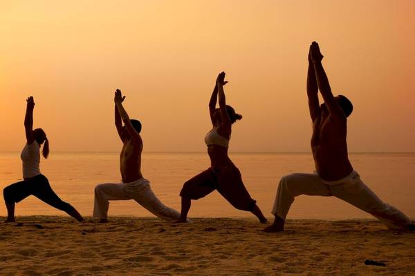 Vier Personen machen Yoga am Strand bei Sonnenuntergang.