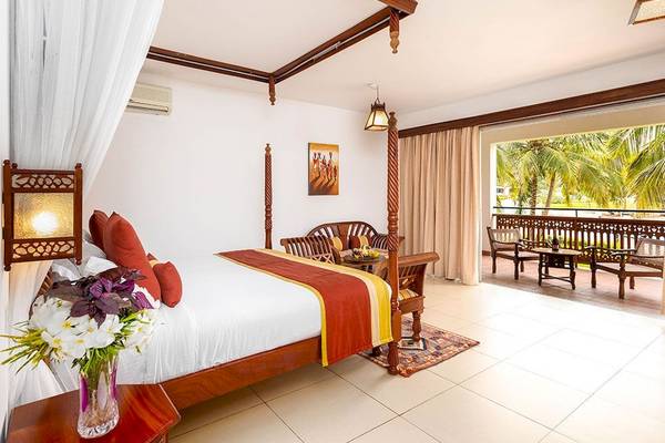 Schlafzimmer im Royal Zanzibar Beach Resort mit Himmelbett, Balkon und Blick auf Palmen.