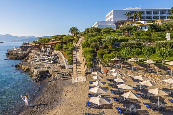 Luftaufnahme des Minos Palace Hotel & Suites am Strand mit vielen Sonnenschirmen und Liegen