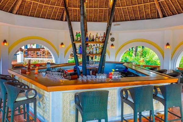 Innenansicht der Bar im Royal Zanzibar Beach Resort mit runden Tischen, Stühlen und einer Bartheke mit Getränken.