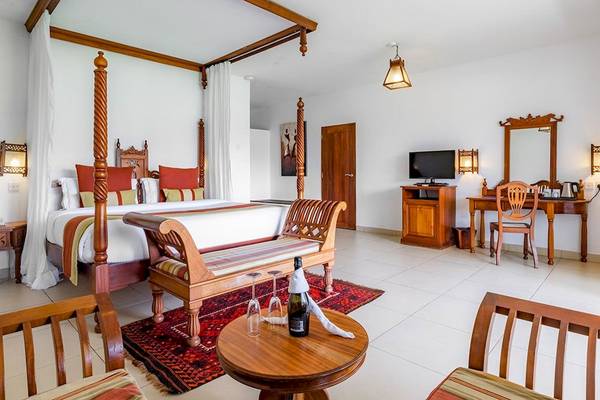 Innenansicht eines luxuriösen Zimmers im Royal Zanzibar Beach Resort mit einem großen Himmelbett, Esstisch und Fernseher.