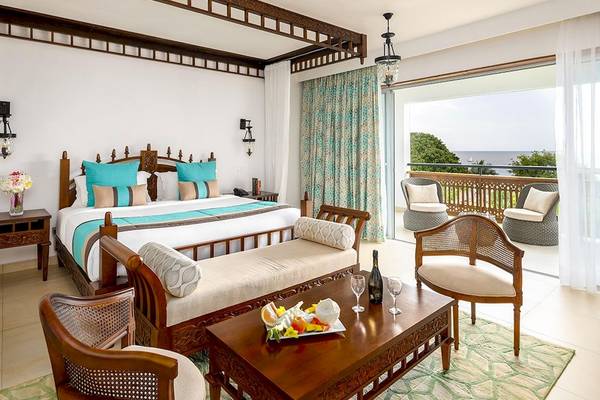 Innenansicht einer Suite im Royal Zanzibar Beach Resort mit Bett, Balkon und Blick auf das Meer.