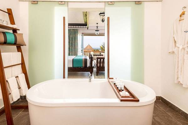 Badezimmer im Royal Zanzibar Beach Resort mit Badewanne, offenem Fenster und Blick auf das Zimmer.