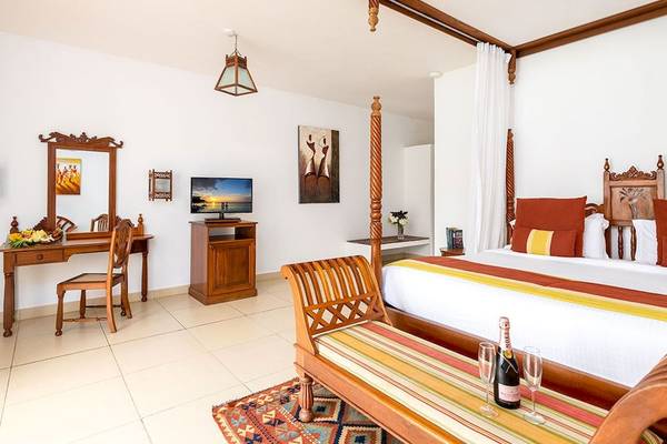 Schlafzimmer im Royal Zanzibar Beach Resort mit Himmelbett, Fernseher, Schreibtisch und Weinflaschen auf dem Tisch.
