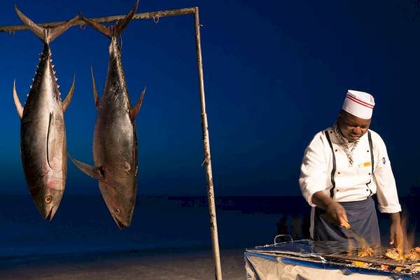 Koch am Grill mit frischen Thunfischen aufgehängt am Strand des Royal Zanzibar Beach Resort