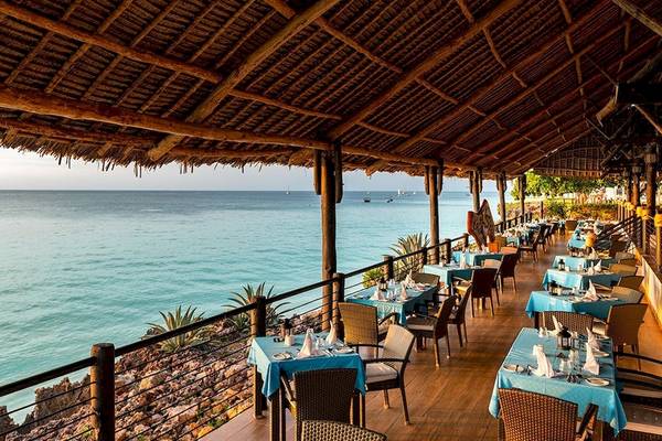 Terrasse des Royal Zanzibar Beach Resorts mit Blick auf das Meer und mehrere gedeckte Tische.