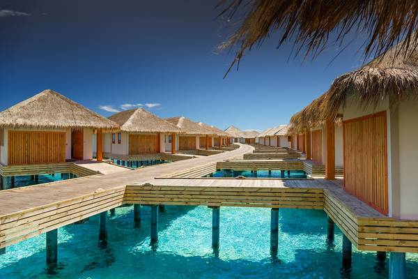 Reihe von Wasserbungalows im Kudafushi Resort & Spa mit hölzernen Stegen über klarem Wasser.