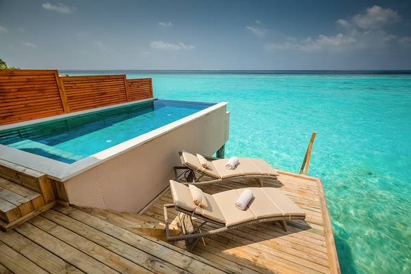 Pool auf Holzplattform am Kudafushi Resort & Spa mit zwei Liegen und Ausblick auf das Meer.