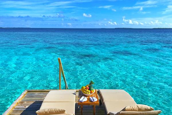 Terrasse des Kudafushi Resort & Spa mit zwei Liegen und Frühstückstisch am Rand des Ozeans