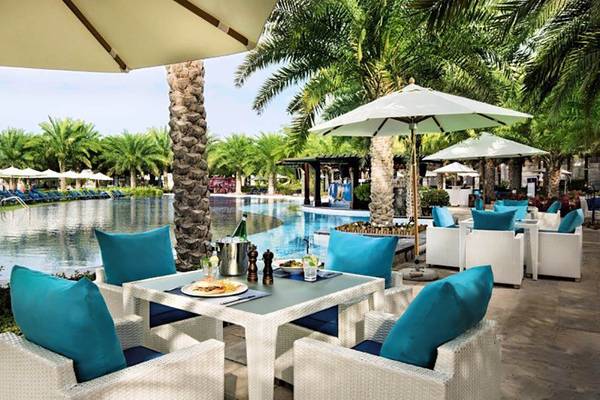 Rixos The Palm Hotel & Suites mit Essbereich am Pool und blauen Kissen und Schirmen.